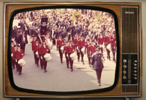 Televisie uit de jaren 60 met afbeelding van slagwerkgroep Echo der Kempen lopend over straat bij evenement