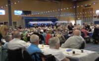 heel veel mensen aan lange tafels nemen deel aan de ziekendag in een sporthal